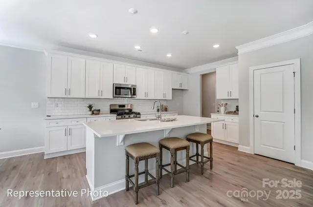 a kitchen with a sink a stove a refrigerator and white cabinets with wooden floor