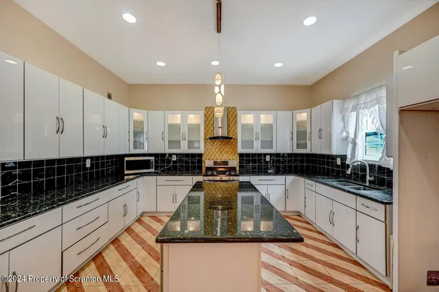 a kitchen with granite countertop a refrigerator a sink and white cabinets