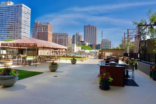 655 West Irving Park Road, Unit 910 Chicago, IL 60613 - Photo 14 of 14 a view of a patio with dining table and chairs under an umbrella with a fire pit