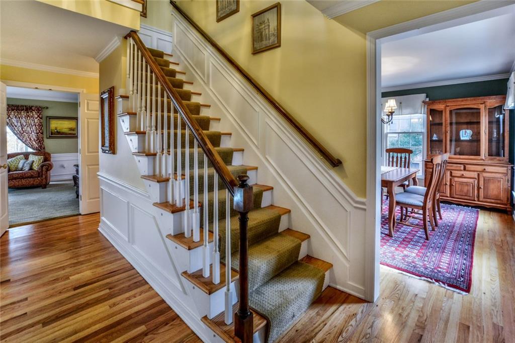 Elegant entry with pristine hardwood floors, wainscoating, crown molding and bright butter color paint. View on right is dining room with 3 windows for natural light and straight back is family room with gas log fireplace and sliding door to screened porch.