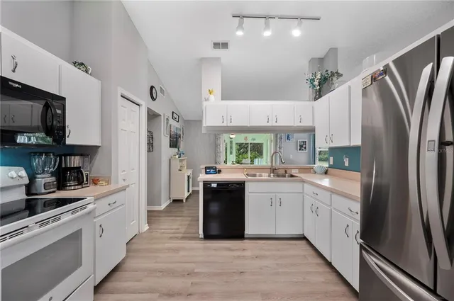 a large white kitchen with stainless steel appliances granite countertop a refrigerator a sink dishwasher a stove and white cabinets with wooden floor