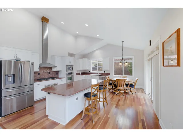 a kitchen with stainless steel appliances granite countertop a refrigerator a sink a stove and a dining table with wooden floor