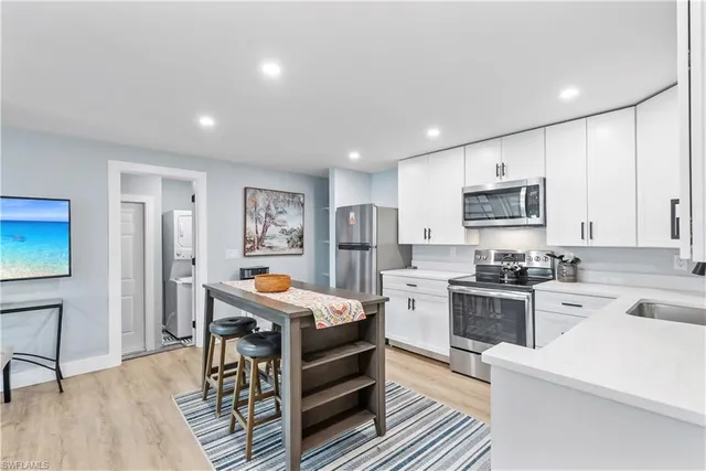 a room with stainless steel appliances kitchen island granite countertop a refrigerator a stove a sink dishwasher and white cabinets with wooden floor