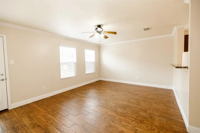 an empty room with wooden floor ceiling fan and windows