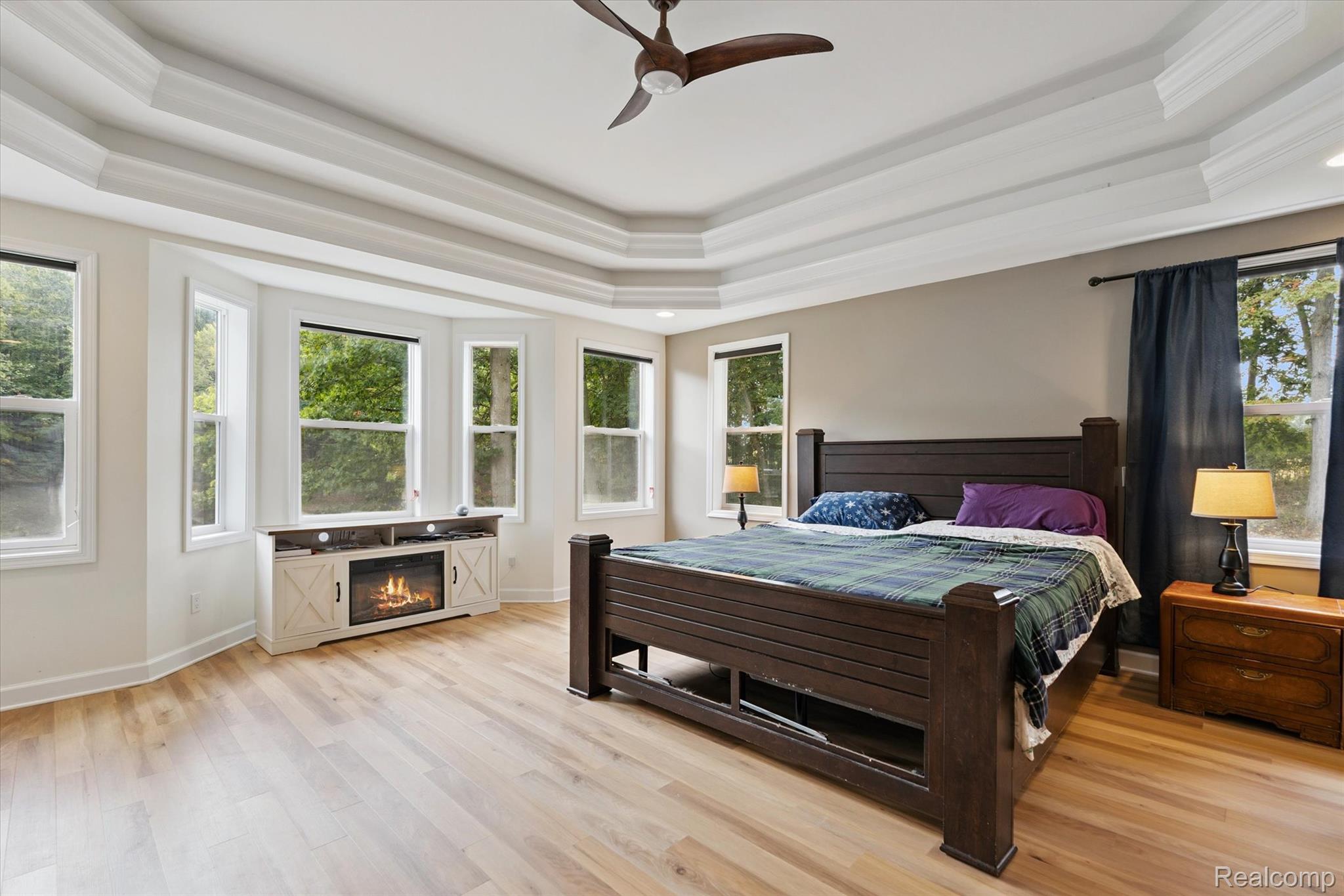 441 West Dryden Road Metamora, MI 48455 - Photo 27 of 62 Bedroom with a tray ceiling, light wood-style flooring, ceiling fan, and a glass covered fireplace