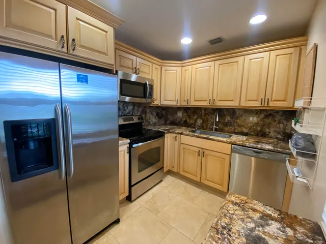 a kitchen with stainless steel appliances granite countertop a refrigerator a stove and a sink