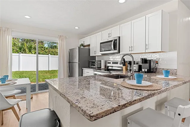 a kitchen with stainless steel appliances granite countertop a table chairs sink and cabinets