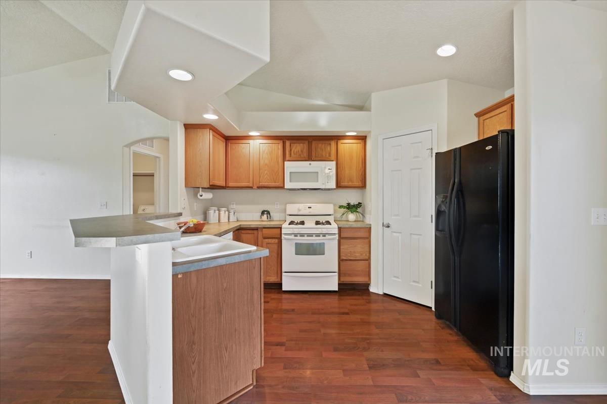 612 Goshawk Avenue Middleton, ID 83644 - Photo 12 of 36 Kitchen with white appliances, a peninsula, wood finish cabinets, dark wood-type flooring, and a kitchen breakfast bar