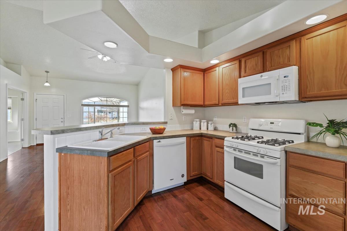 612 Goshawk Avenue Middleton, ID 83644 - Photo 14 of 36 Kitchen featuring white appliances, a peninsula, dark wood finished floors, wood finish cabinetry, and hanging light fixtures