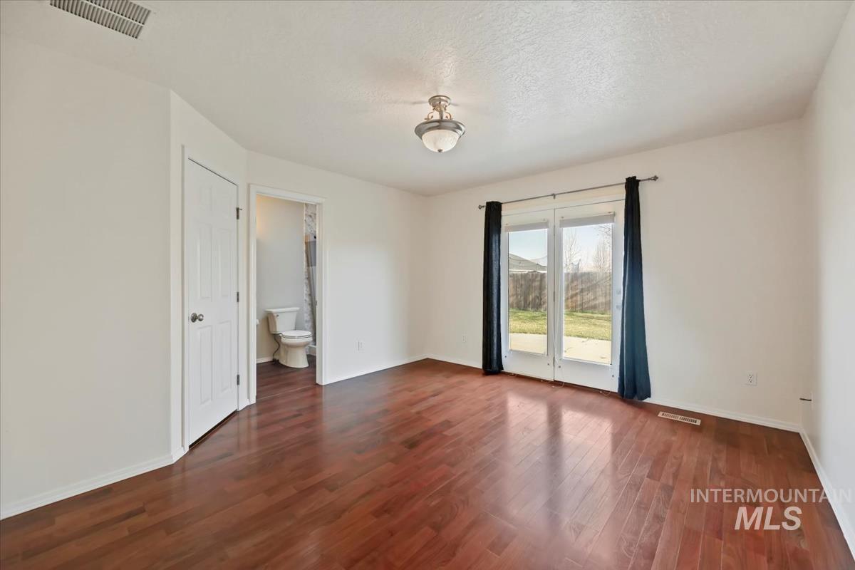 612 Goshawk Avenue Middleton, ID 83644 - Photo 16 of 36 Unfurnished bedroom with access to outside, dark wood-style flooring, ensuite bath, and a textured ceiling