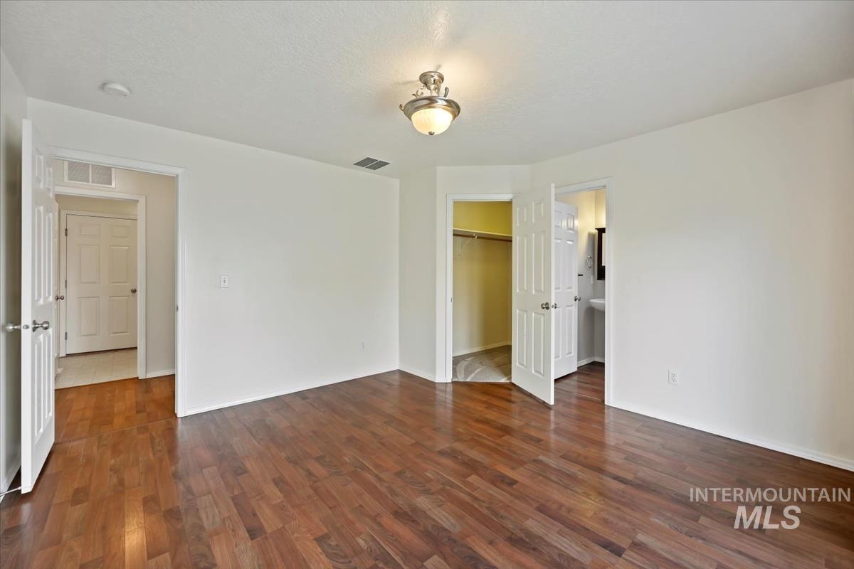 612 Goshawk Avenue Middleton, ID 83644 - Photo 18 of 36 Unfurnished bedroom featuring a spacious closet, dark wood-type flooring, connected bathroom, and a textured ceiling
