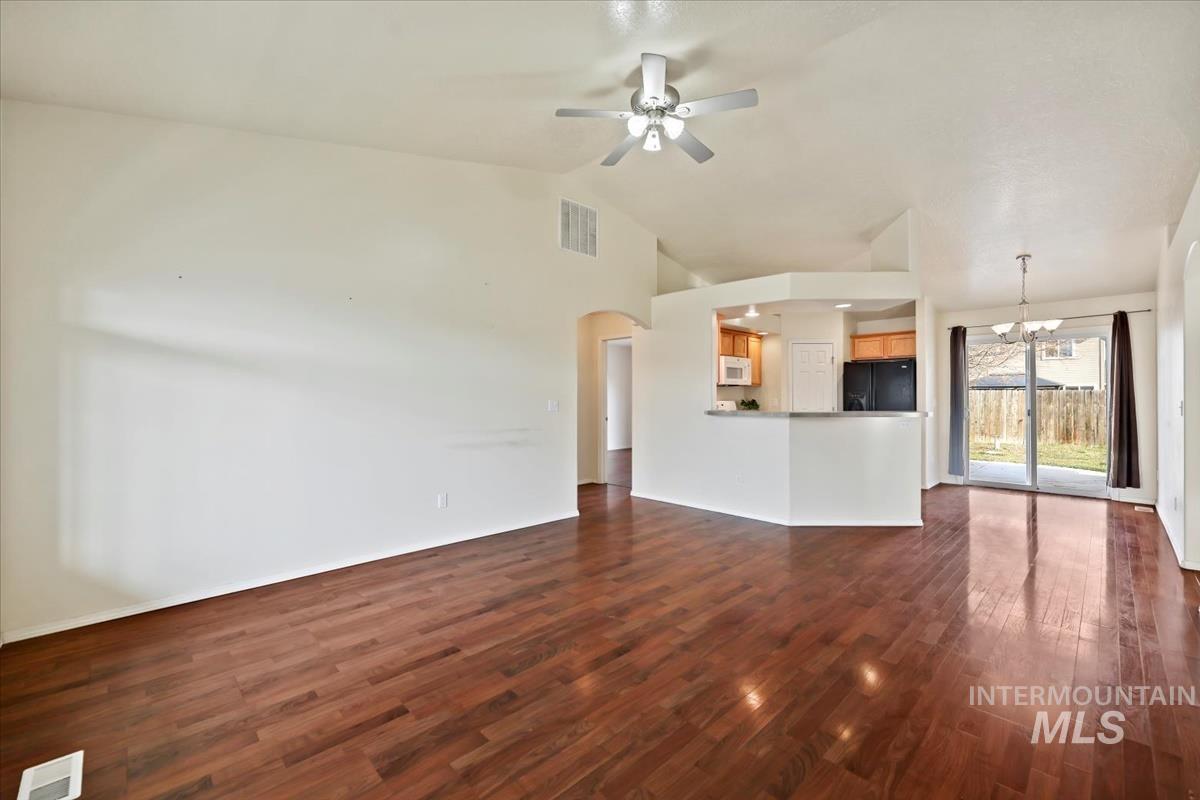 612 Goshawk Avenue Middleton, ID 83644 - Photo 5 of 36 Unfurnished living room featuring a ceiling fan, hanging lights, arched walkways, dark wood-type flooring, and vaulted ceiling