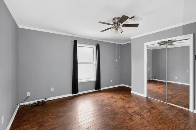 a view of an empty room with wooden floor and a ceiling fan