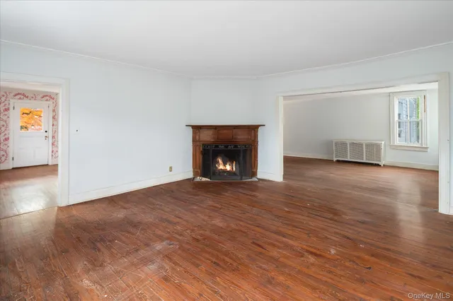 a view of an empty room with wooden floor fireplace and a window