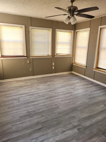 an empty room with wooden floor fan and windows