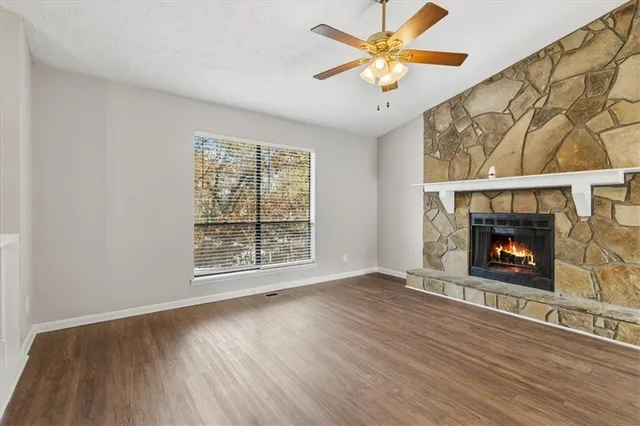 an empty room with windows a fireplace a ceiling fan and wooden floor