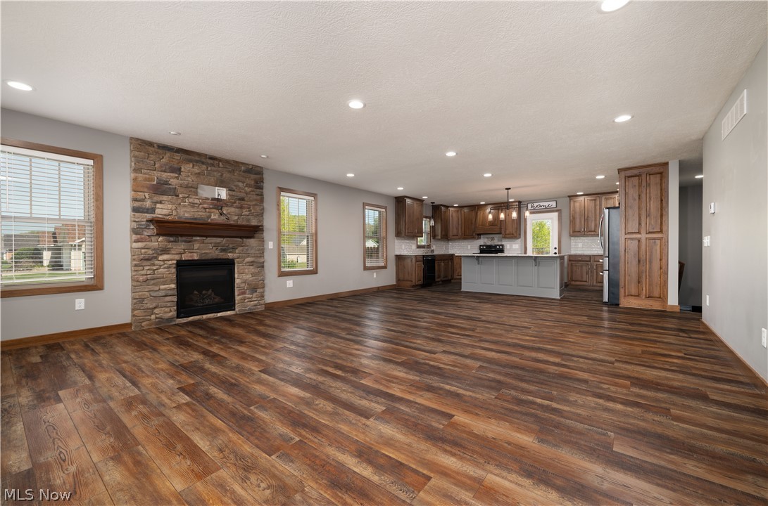 3515 Eastport Road Southeast Dennison, OH 44621 - Photo 9 of 41 Open-concept living area featuring wood-finish flooring, a stone-faced fireplace with a wooden mantel, recessed lighting, and a kitchen with wood cabinetry, a light gray island, and stainless steel appliances