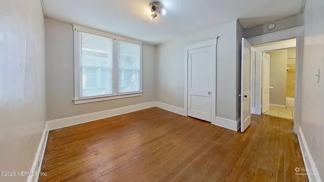 a view of an empty room with wooden floor and a window