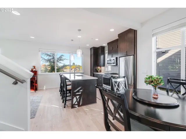 a kitchen with stainless steel appliances kitchen island granite countertop a refrigerator a stove a sink a dining table and chairs with wooden floor