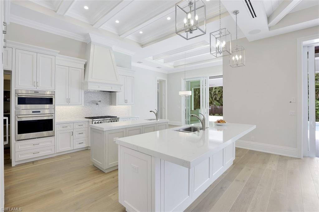 1670 Crayton Road Naples, FL 34102 - Photo 9 of 26 a large white kitchen with stainless steel appliances granite countertop a stove oven a sink dishwasher and white cabinets with wooden floor