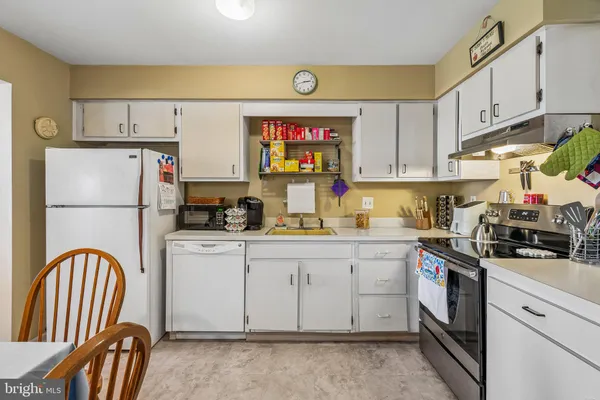 a kitchen with stainless steel appliances granite countertop a stove a sink dishwasher a refrigerator a stove and white cabinets with wooden floor