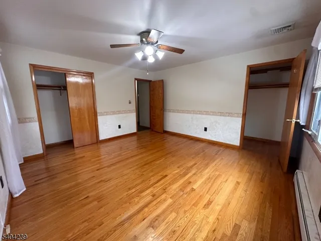 a view of an empty room with wooden floor and a ceiling fan