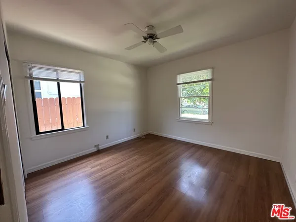 an empty room with wooden floor windows and fan