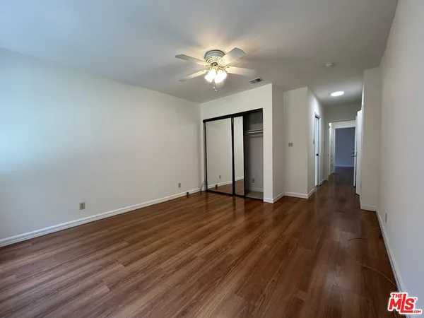 a view of an empty room with wooden floor and a ceiling fan
