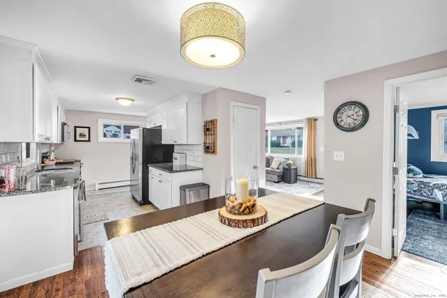 a living room with stainless steel appliances furniture a clock and a view of kitchen