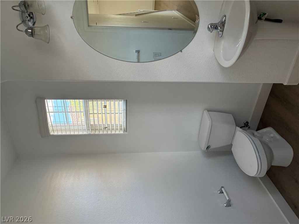 7727 Pista Way Las Vegas, NV 89179 - Photo 9 of 12 A well-lit bathroom features a vanity, mirror, toilet, and window with blinds.