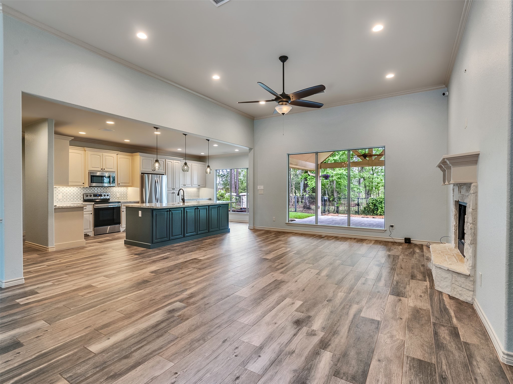 18005 Cindy Lane Conroe, TX 77302 - Photo 7 of 49 This spacious open-concept living area features hardwood flooring, a modern kitchen with a large island, stainless steel appliances, and pendant lighting. The room has a cozy fireplace and large windows offering a view of the backyard, perfect for natural light and entertaining.