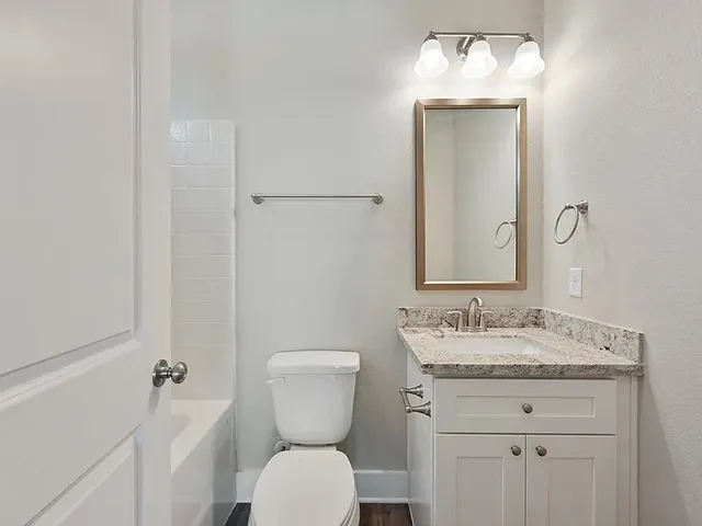 a bathroom with a granite countertop toilet a sink and a mirror