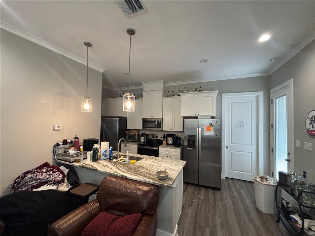407 Ash Street College Station, TX 77840 - Photo 5 of 14 Kitchen featuring appliances with stainless steel finishes, white cabinetry, ornamental molding, light stone counters, and dark wood-style floors