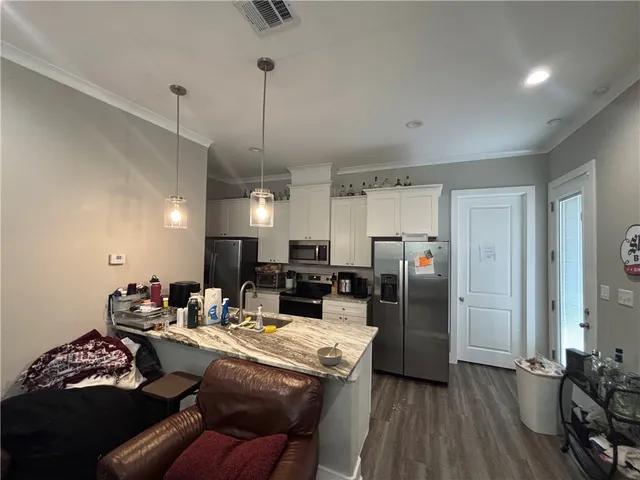 a kitchen with stainless steel appliances kitchen island granite countertop a refrigerator a stove and white cabinets with wooden floor