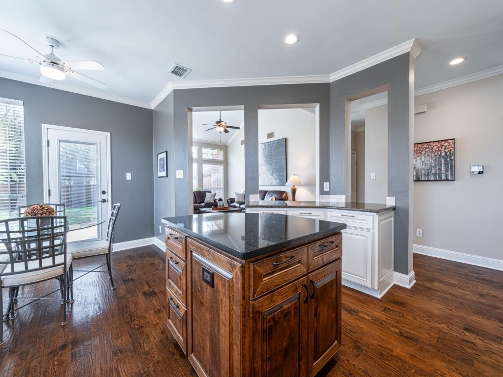 5504 Baton Rouge Boulevard Frisco, TX 75035 - Photo 18 of 36 Two tone kitchen with dark stone counters, dark wood-style floors, a center island, ornamental molding, and two tone color scheme