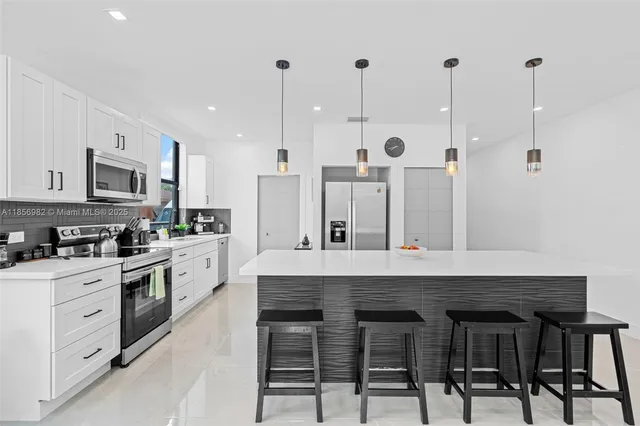 a kitchen with stainless steel appliances kitchen island a table chairs sink and cabinets