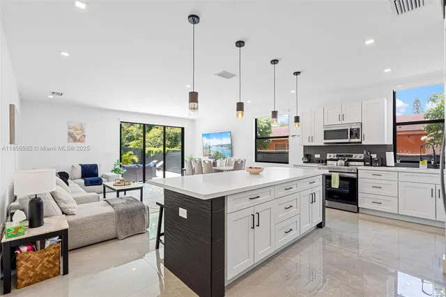 a large white kitchen with stainless steel appliances granite countertop a stove a sink dishwasher a refrigerator and white cabinets with wooden floor