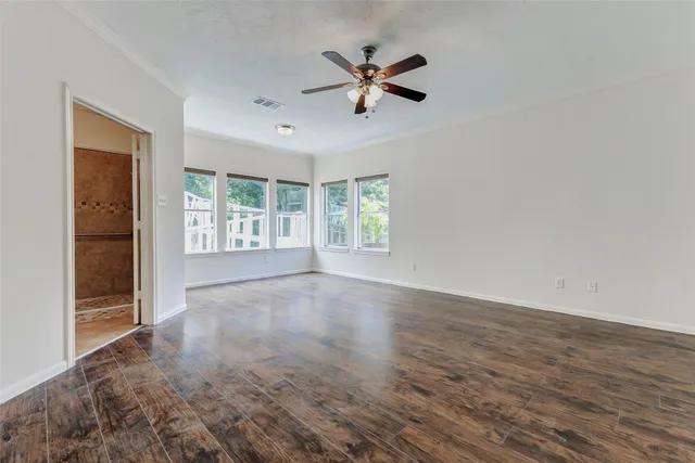 an empty room with wooden floor chandelier fan and windows