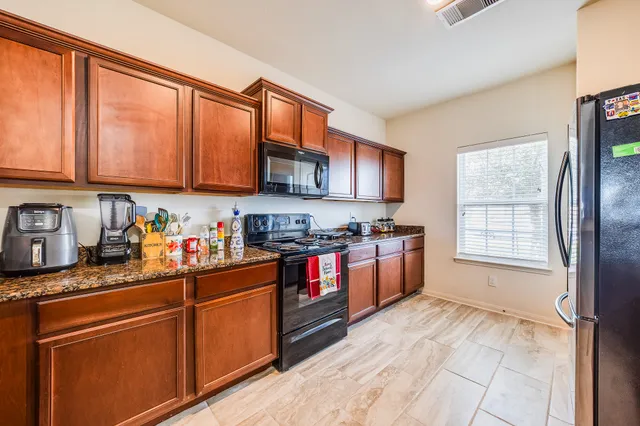 a kitchen with stainless steel appliances granite countertop a stove top oven a sink dishwasher and a refrigerator with wooden cabinets