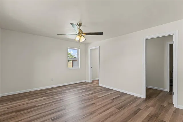 a view of an empty room with wooden floor and a ceiling fan