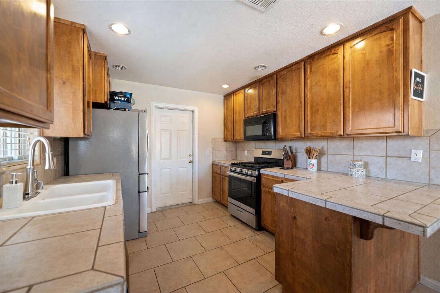 7562 Inca Trail Yucca Valley, CA 92284 - Photo 16 of 30 a kitchen with a sink a stove top oven a refrigerator cabinets and a dining table