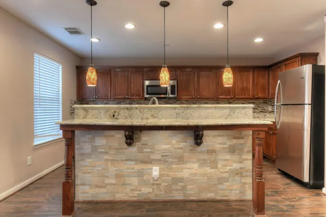 a kitchen with kitchen island granite countertop wooden cabinets a refrigerator a sink and a stove