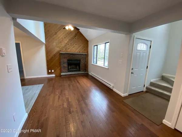 a view of an empty room with wooden floor fireplace and a window