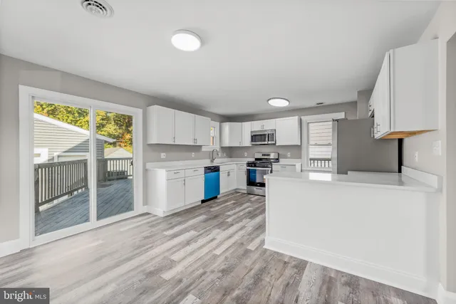 a kitchen with stainless steel appliances granite countertop a coffee maker a sink a refrigerator with white cabinets and wooden floor