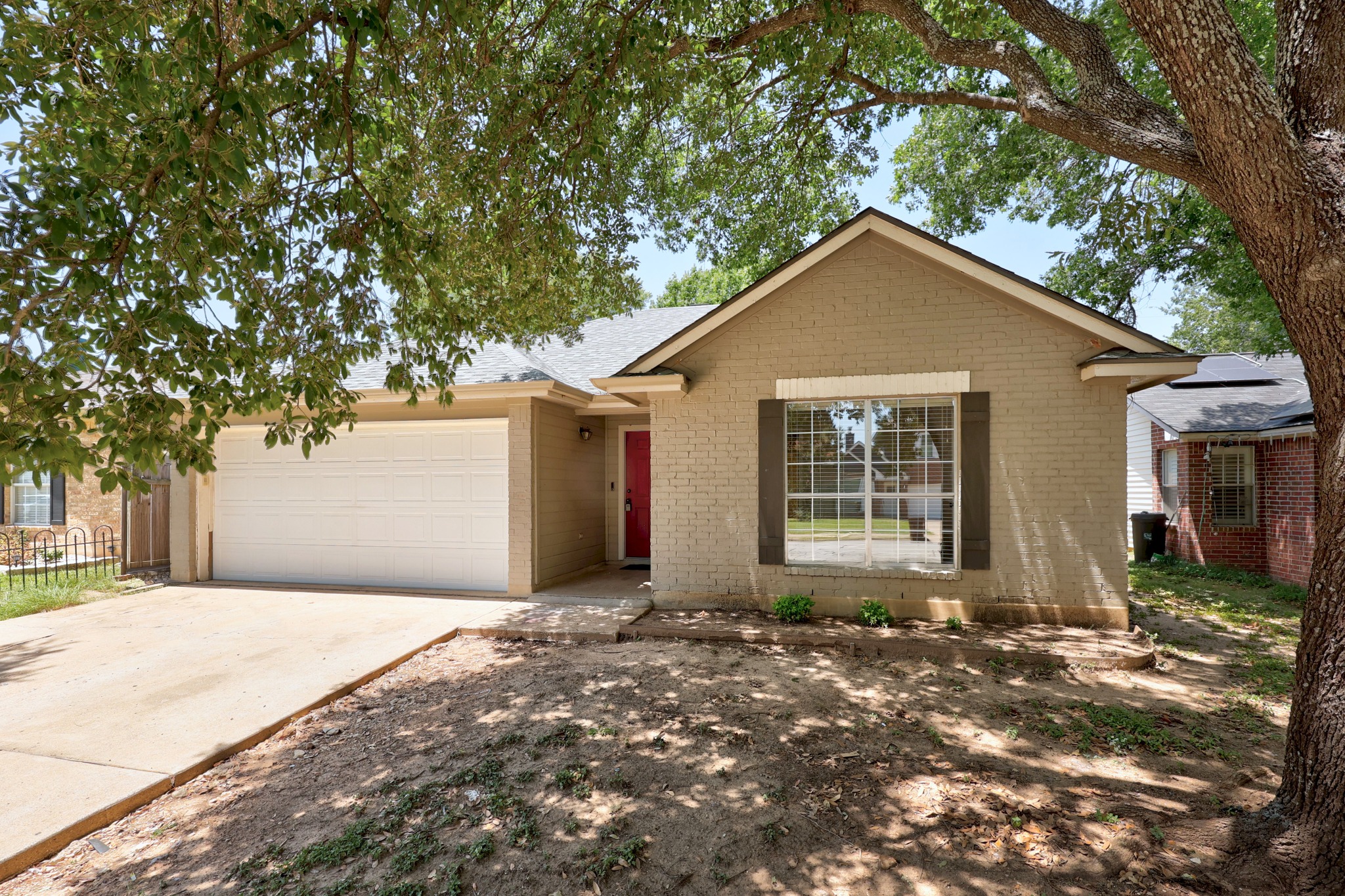 1806 Rusty Nail Loop Round Rock, TX 78681 - Photo 3 of 28 A welcoming brick exterior with a bright red door and attached garage, nestled under mature trees.