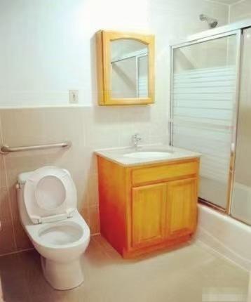 35-06 Leavitt Street, Unit 7F Queens, NY 11354 - Photo 4 of 5 Bathroom with vanity, shower / bath combination with glass door, and wainscoting