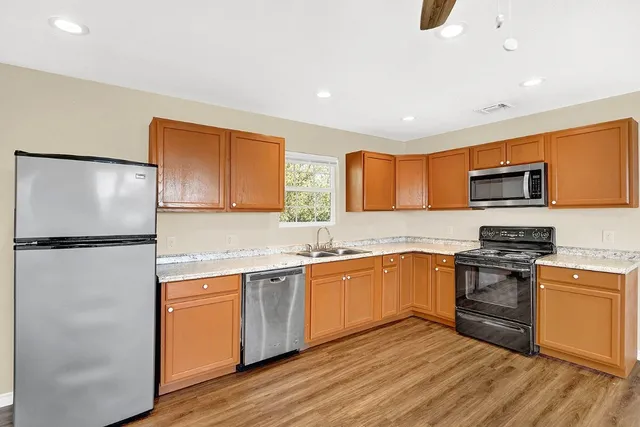 a kitchen with stainless steel appliances granite countertop a refrigerator a stove top oven a sink and dishwasher with wooden floor