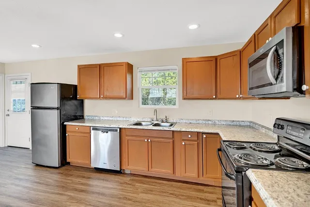 a kitchen with stainless steel appliances granite countertop a stove top oven a refrigerator a sink and dishwasher with wooden floor