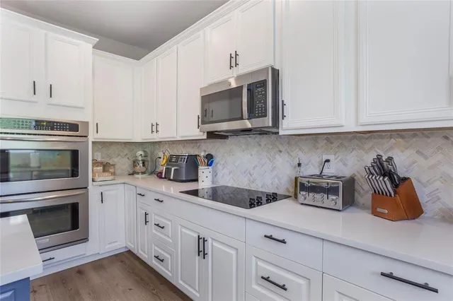 a kitchen with stainless steel appliances granite countertop white cabinets a stove a microwave and a sink