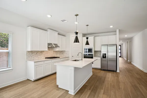 a large kitchen with stainless steel appliances kitchen island granite countertop a stove a sink a refrigerator and white cabinets with wooden floor